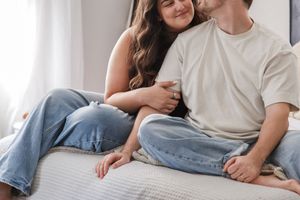 A couple relaxing together on a white bed wearing casual clothing and denim.