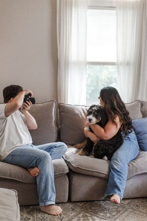 A couple cuddles with their black and white dog on a comfortable gray sofa.