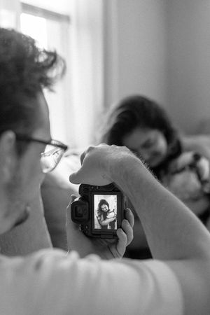 A photographer holds a digital camera displaying a preview image on its LCD screen in black and white.