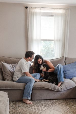 A couple and their dog share playful moments on a plush gray couch in a minimalist living room.