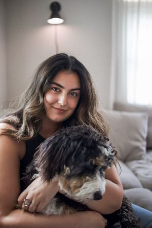 A person sits on a couch holding a fluffy black and white dog in a cozy room with natural lighting.