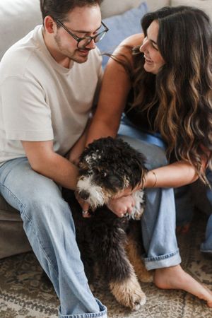 Couple sitting on couch petting their black and white shaggy dog while sharing an intimate moment together.