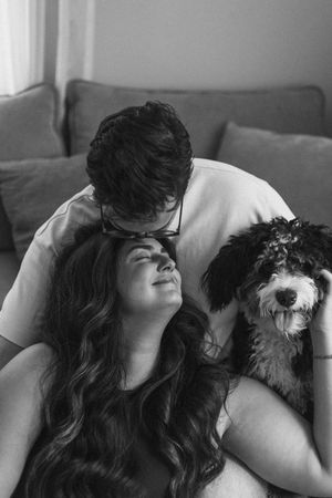A couple relaxes on a couch with their fluffy black and white dog in a casual home setting.
