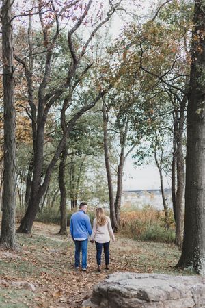 Couple walking together on a scenic autumn trail through wooded area with fallen leaves.