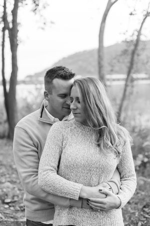 A romantic black and white portrait of a couple embracing outdoors in sweaters among trees.