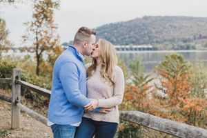 A couple shares a romantic moment on an autumn overlook with colorful fall foliage and a lake view in the background.