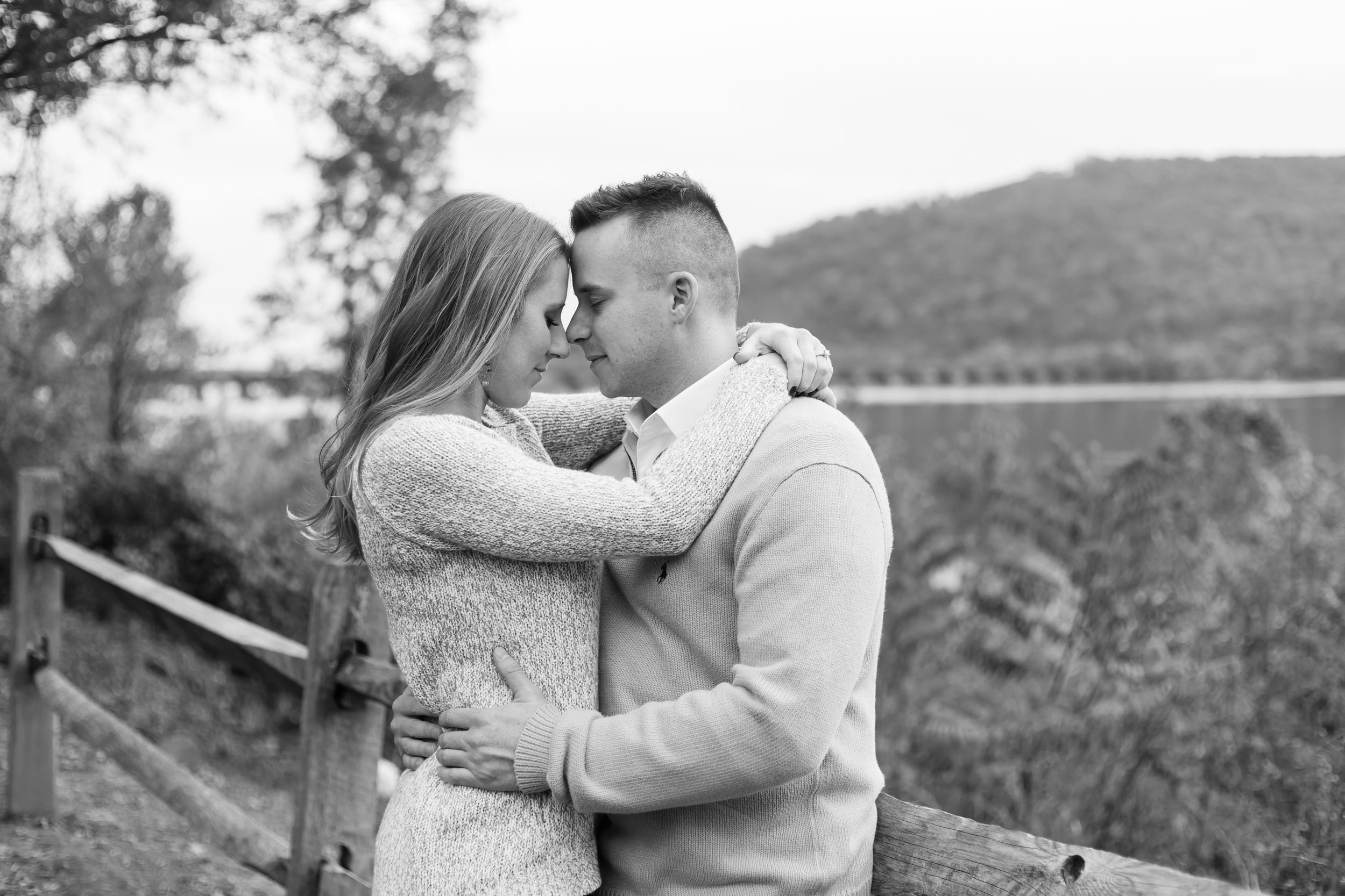 A couple shares a romantic moment while posing for engagement photos in a scenic mountain setting during fall.