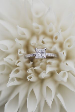 A sparkling diamond engagement ring nestled in the center of a white dahlia flower.