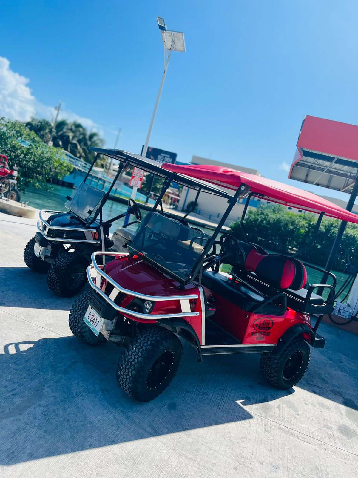 A row of black and red golf carts or utility vehicles parked on a beach with sand and water in the background.