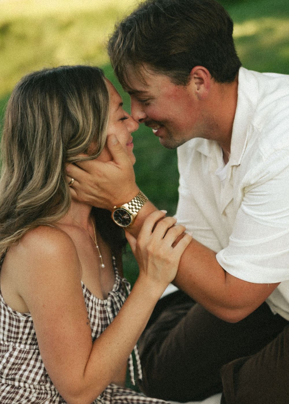 Romantic couple sharing an intimate moment outdoors, man holding woman's face, both smiling and leaning in close.