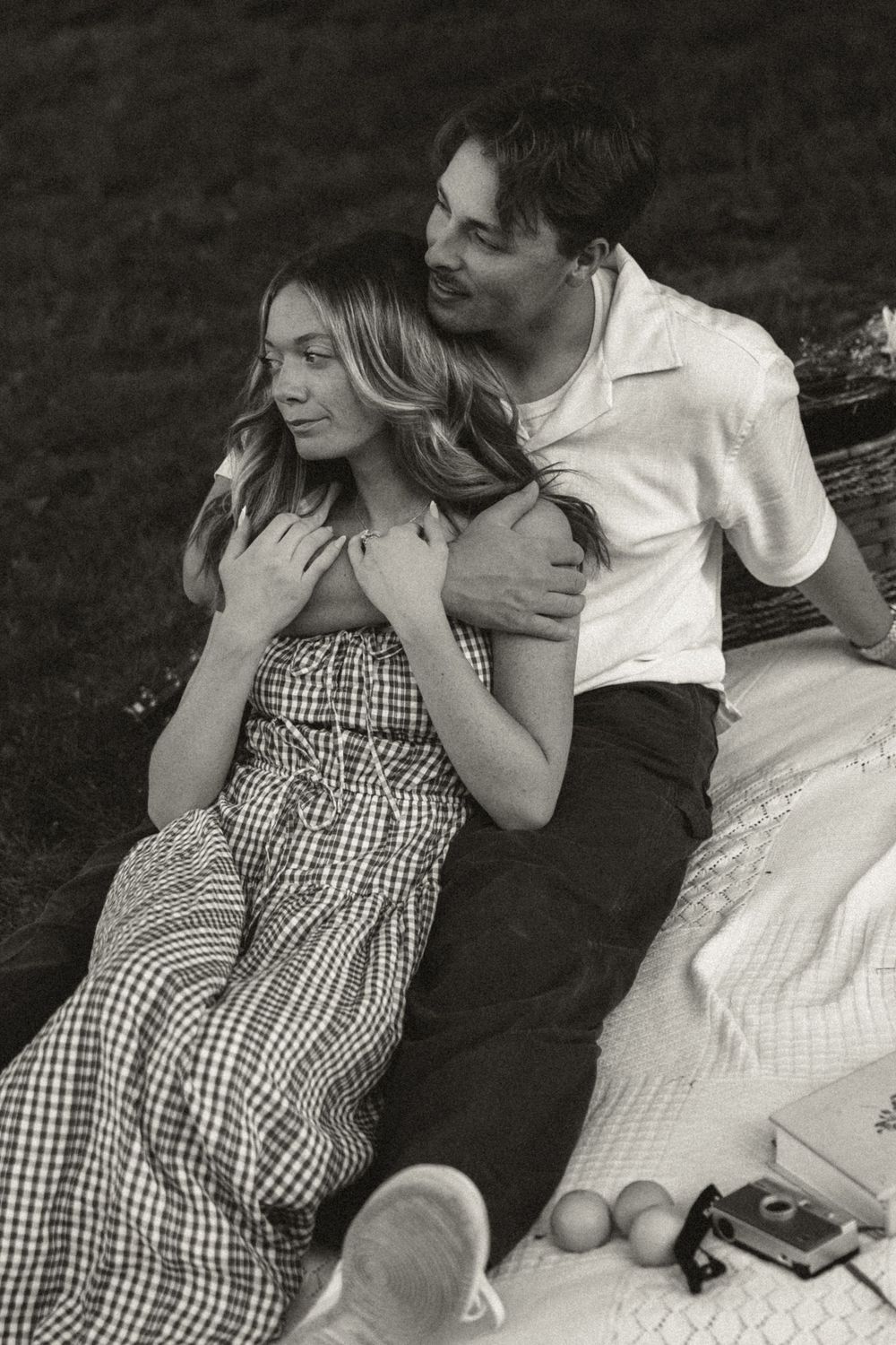 Black and white photo of a couple sharing a tender moment on a picnic blanket outdoors.