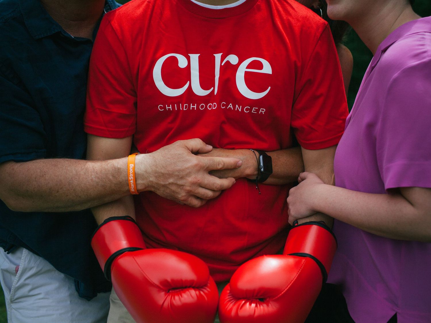 Two people wearing red and pink shirts sit together with boxing gloves during a cancer awareness event.