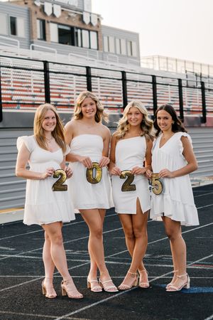 Group wearing white dresses holding 2023 numbers on a track field.