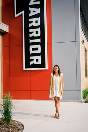 Group poses in white dresses against a red building exterior with black signage.