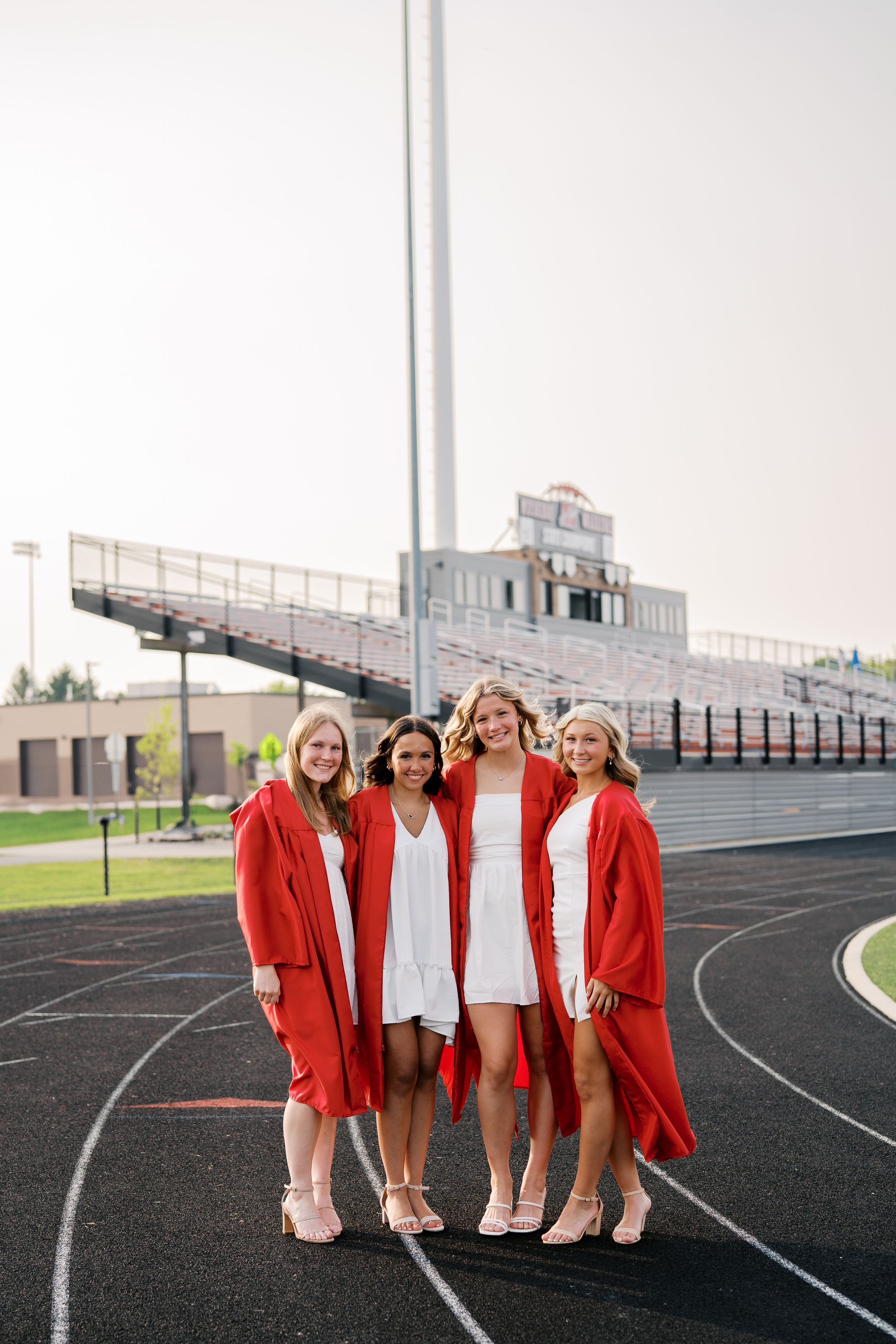 Group wearing red graduation gowns pose together on a running track at a school stadium.