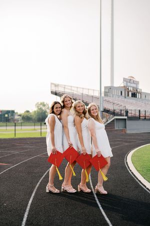 Friends in matching white outfits and red bows pose playfully on a running track.