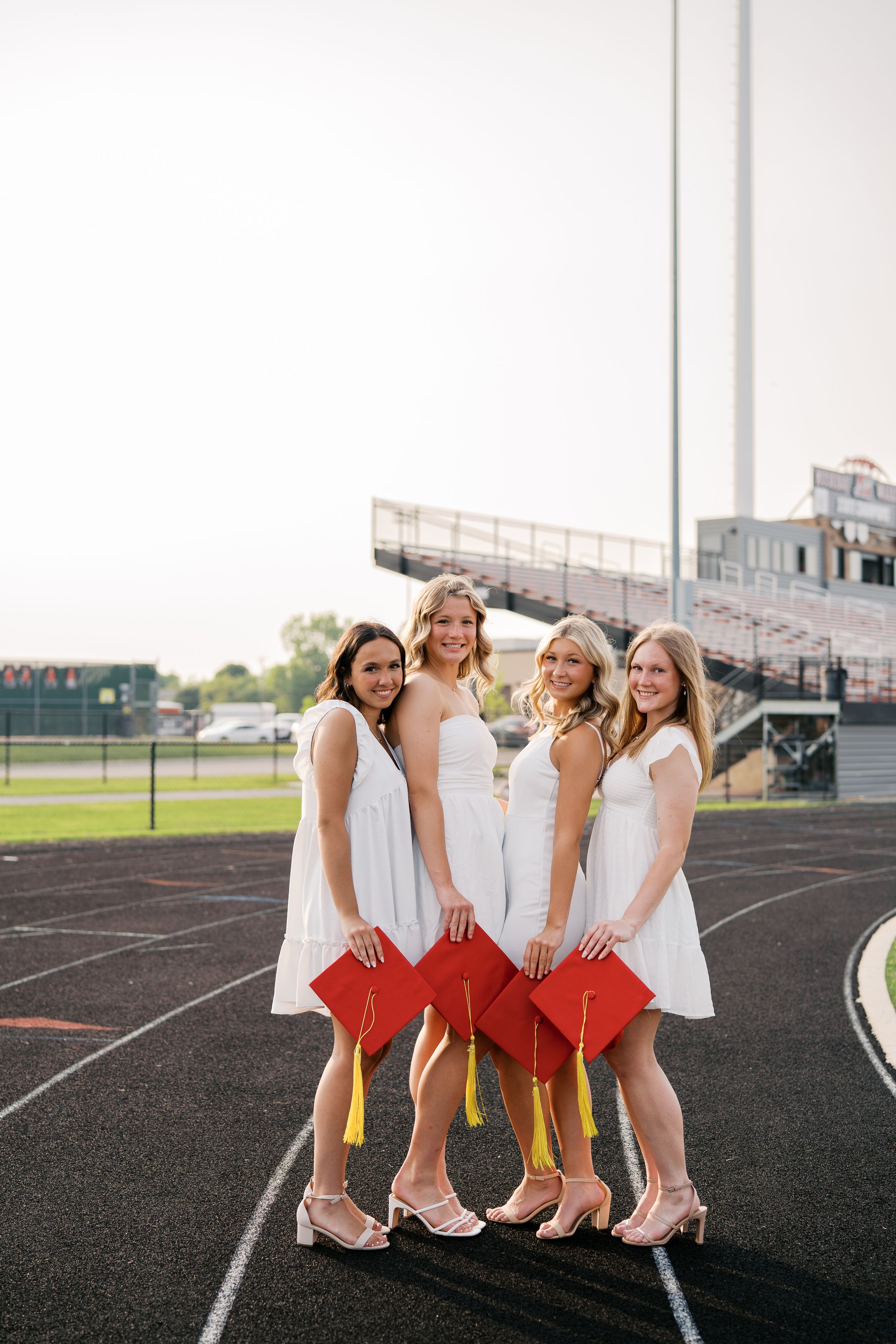 Friends in coordinated white and red outfits laugh together while posing on an outdoor running track.