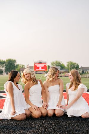 Group sits together on black track surface wearing coordinated white outfits.
