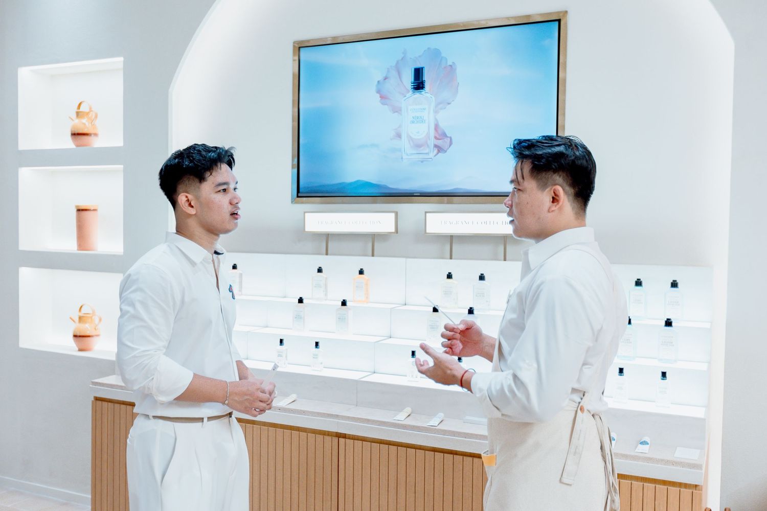 Two men in white uniforms conversing in a modern retail store with product displays and a screen.