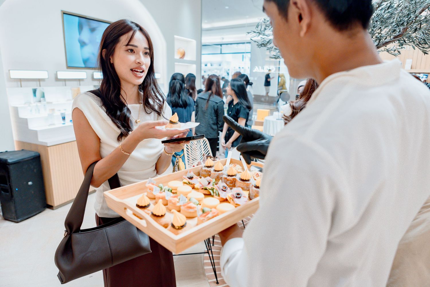 Woman gesturing at a tray of appetizers offered by a server at an elegant retail store event.