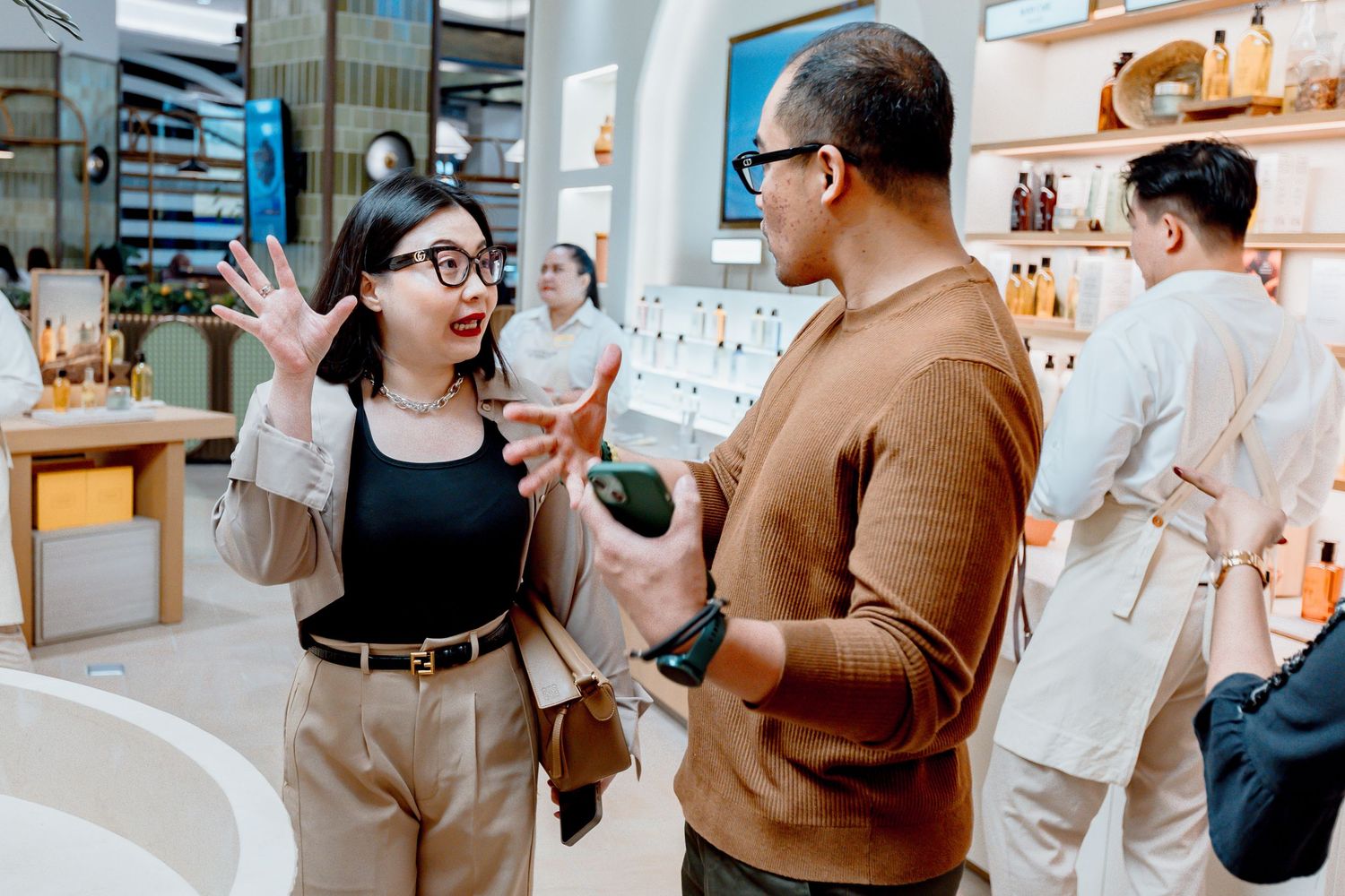 Two people having an animated conversation in a modern retail store with shelves of products in the background.