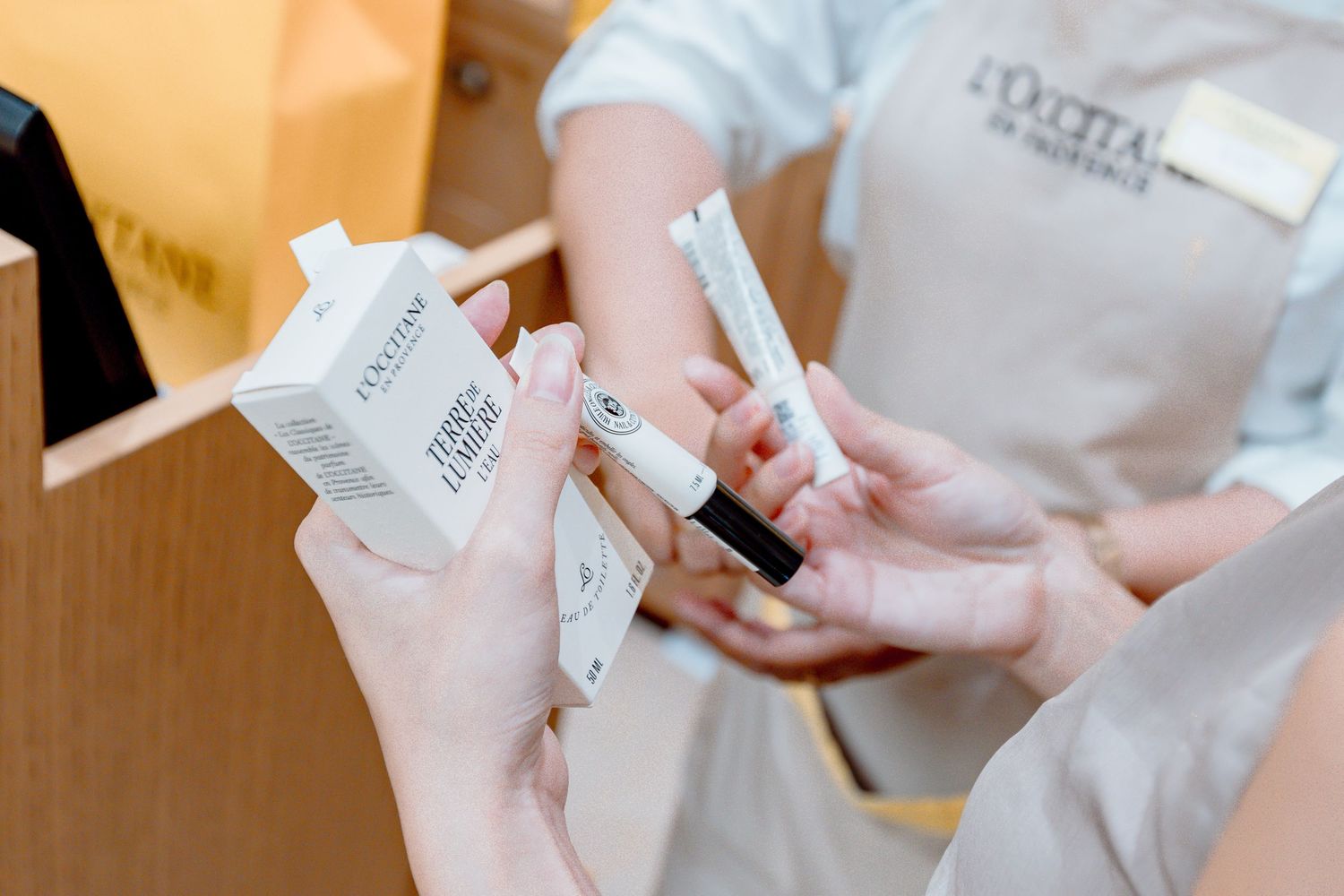 L'Occitane store employee handing skincare products to a customer during an in-store consultation.