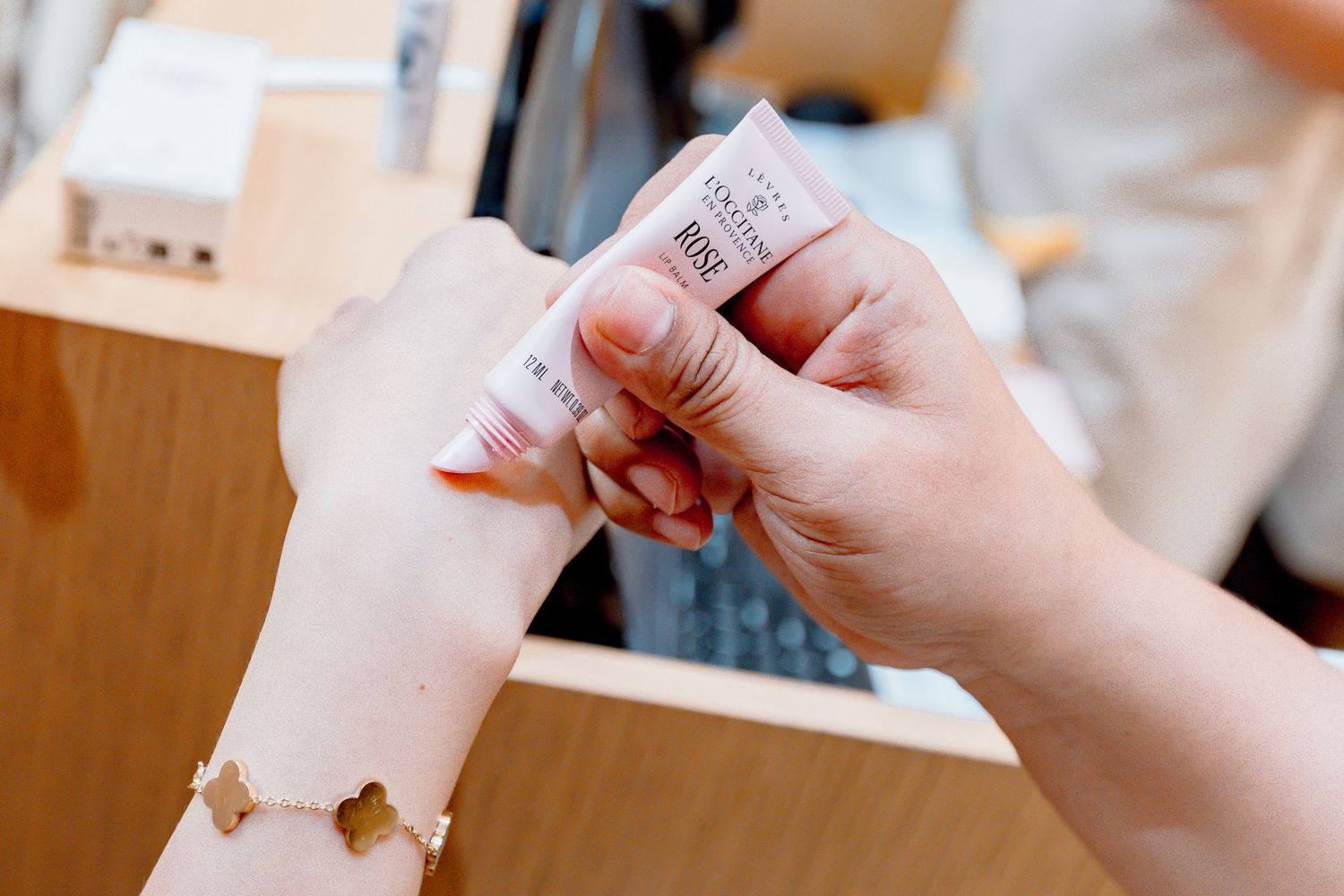 A beauty consultant applies pink lip product to a customer's hand during a cosmetic store consultation.