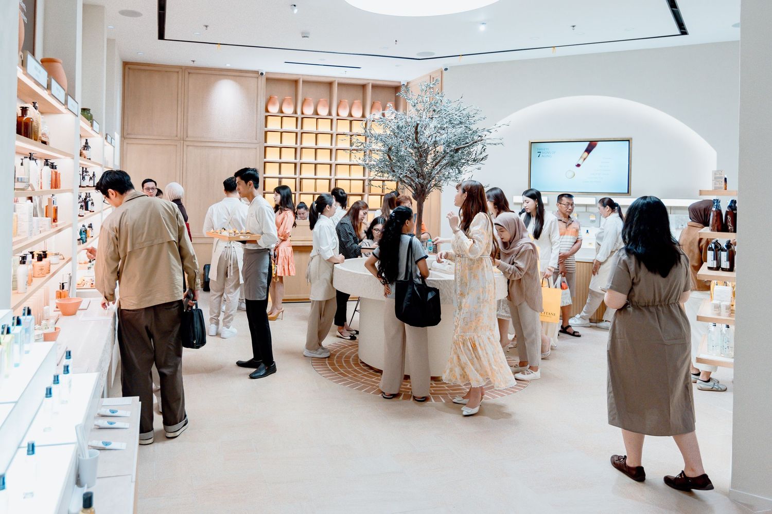 Customers browsing skincare products in a modern, minimalist retail store with white shelves and a decorative tree centerpiece.