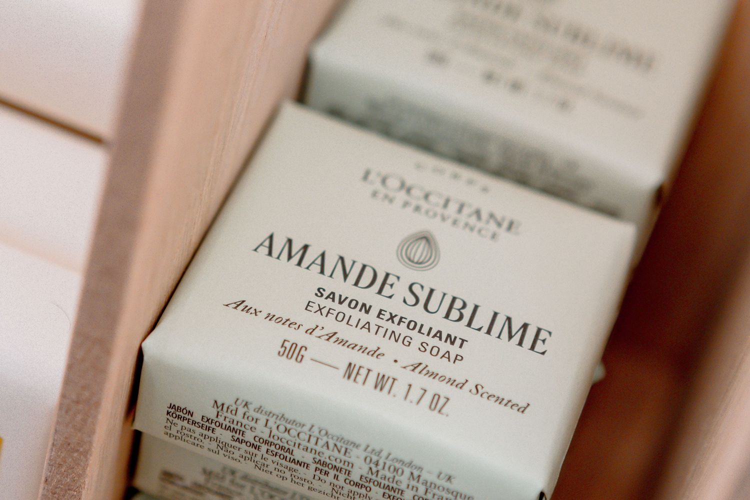 L'Occitane Amande Sublime exfoliating soap bars in elegant packaging displayed in a wooden box.