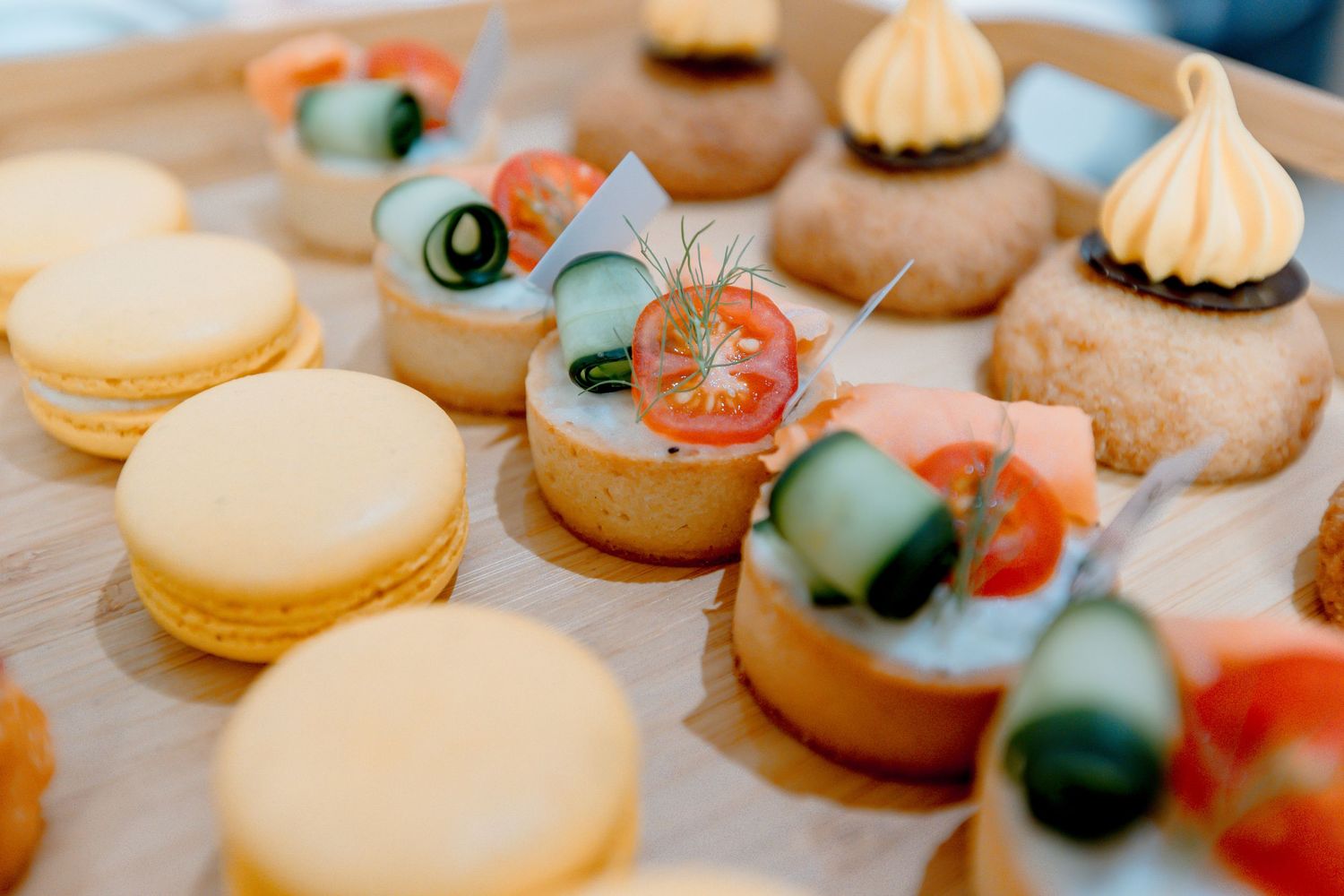 Elegant assortment of French macarons and savory tartlets topped with fresh vegetables on a wooden serving board.