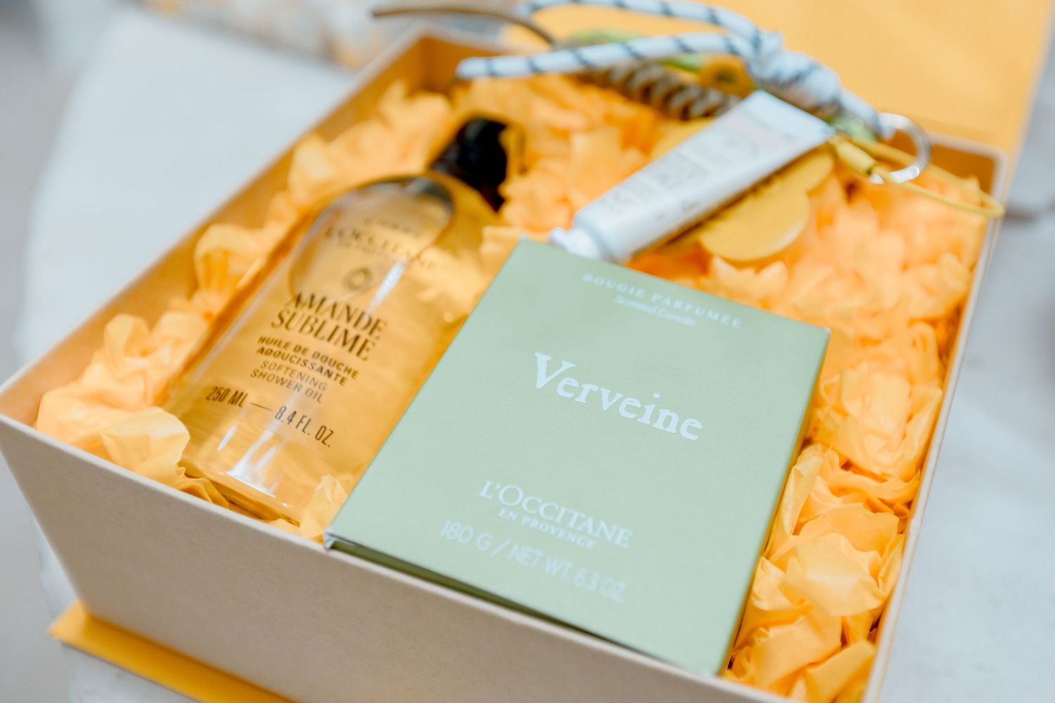 L'Occitane gift box with Verveine soap and Amande Sublime body oil nestled in orange tissue paper.