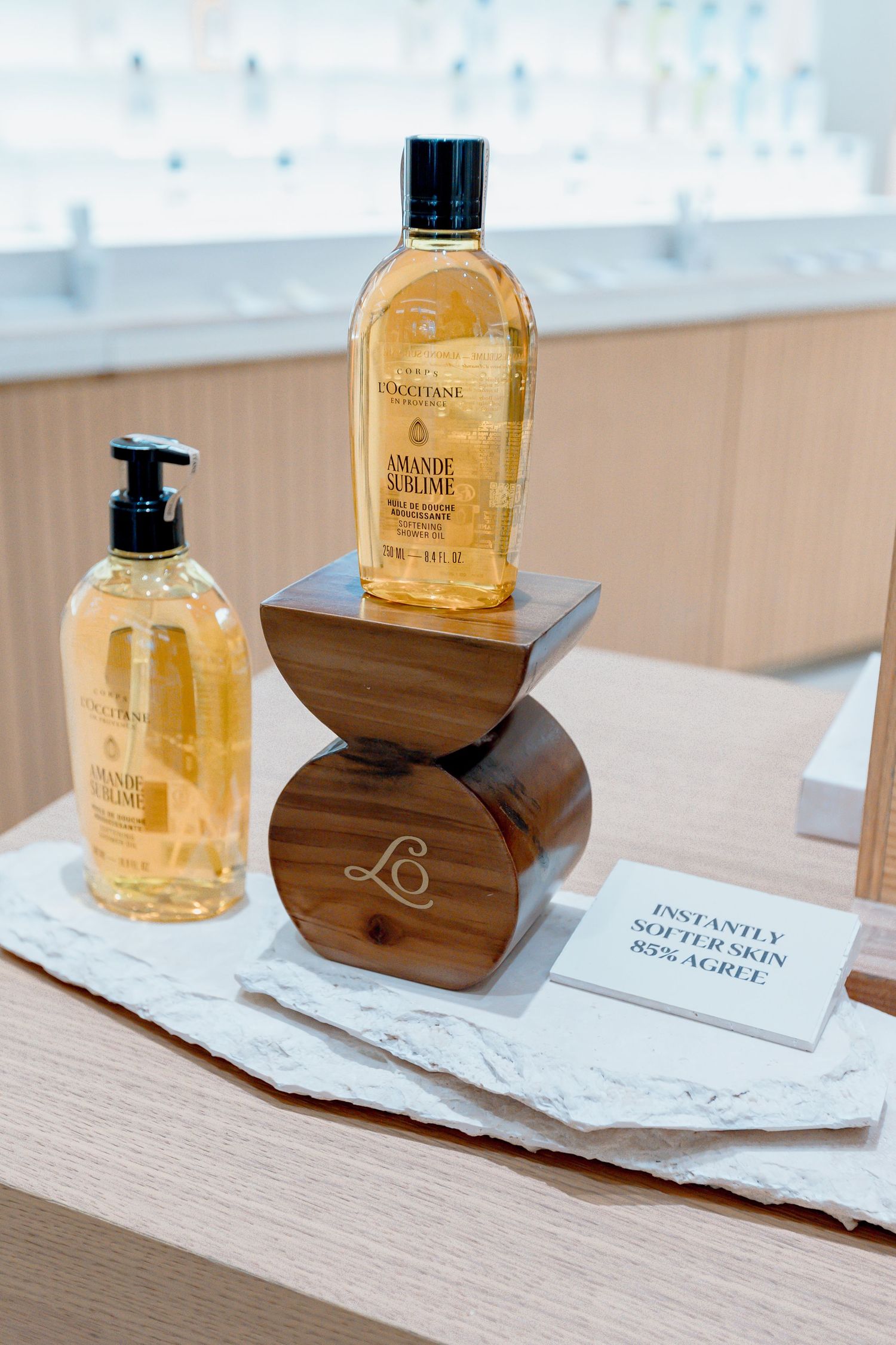 L'Occitane Amande Sublime shower oil and hand soap displayed on wooden blocks in a retail store.