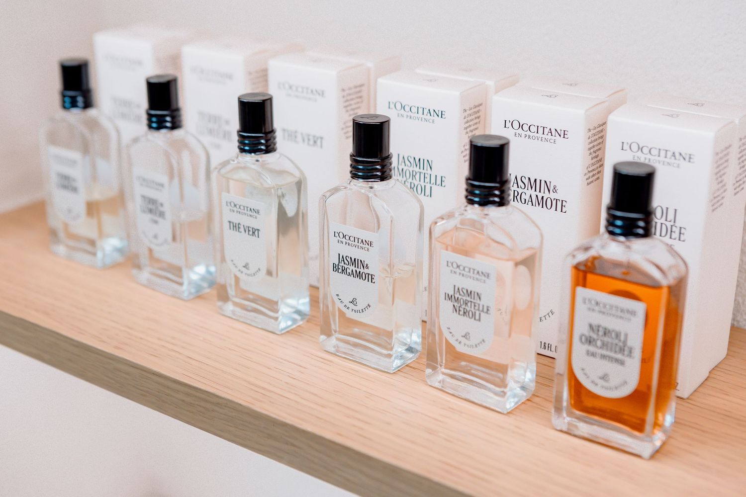 L'Occitane perfume bottles displayed on a wooden shelf, featuring jasmine and other fragrances in clear glass bottles.