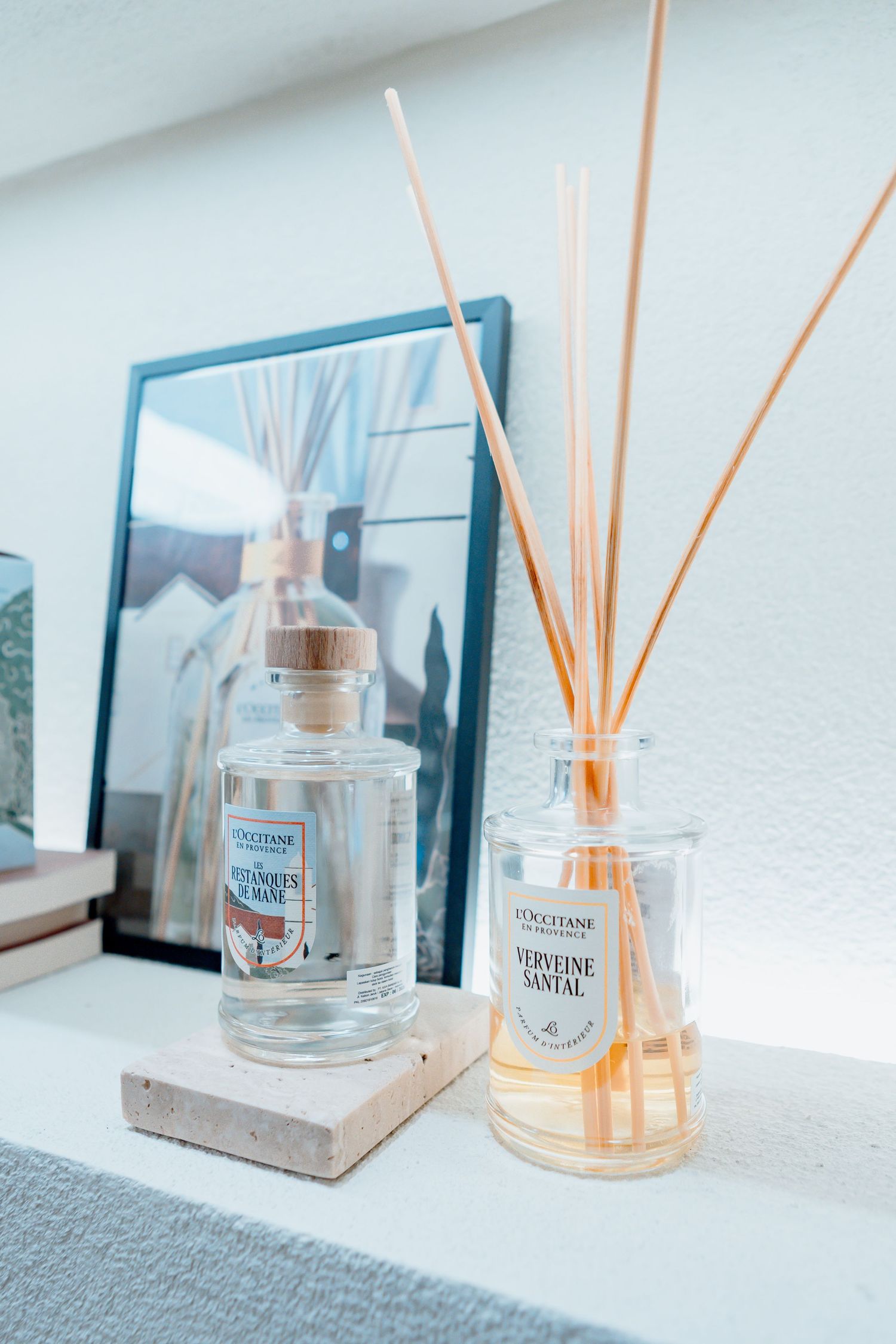 L'Occitane reed diffusers in Verveine Santal scent displayed on a white shelf with a framed photo.