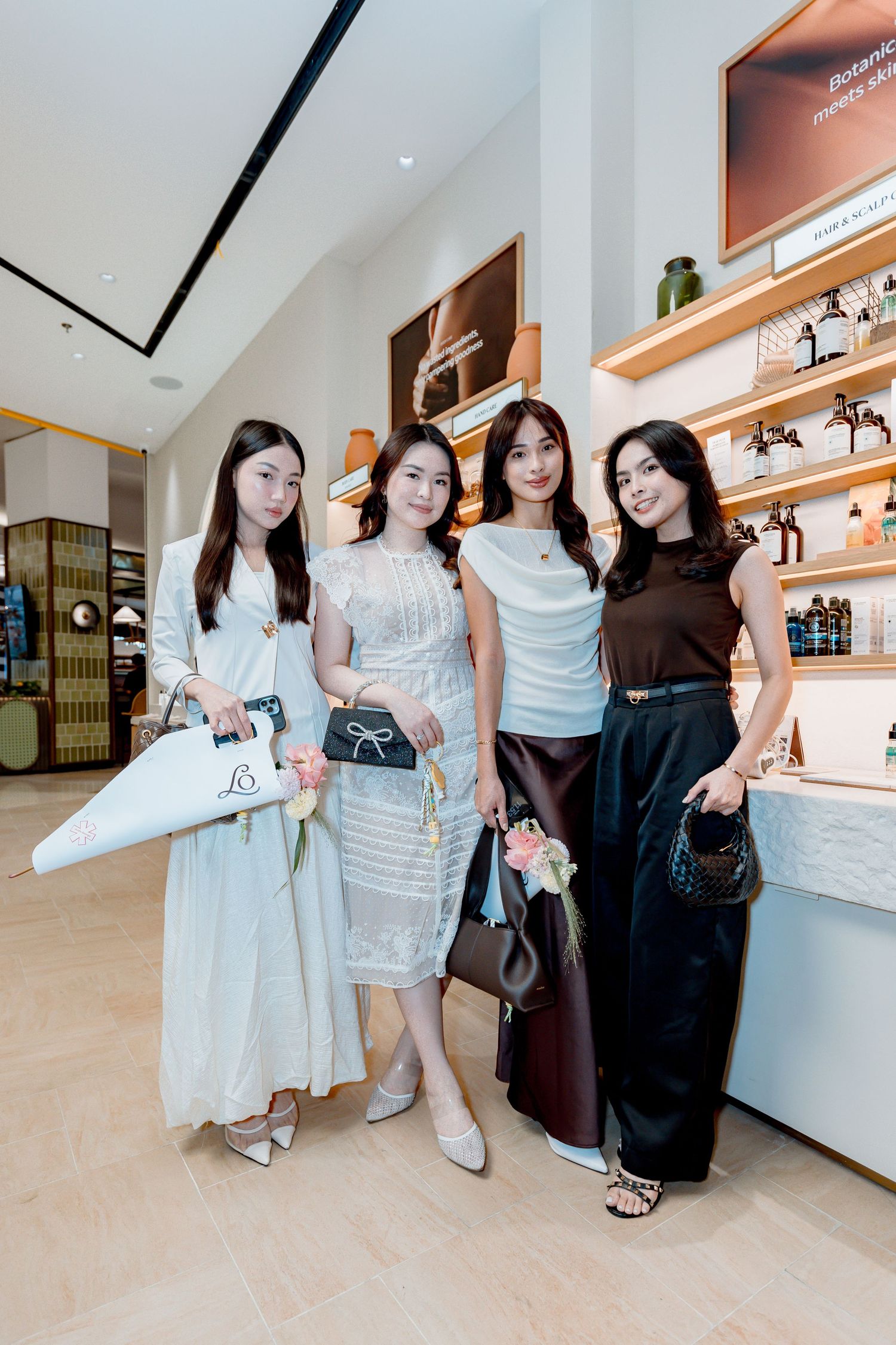 Four stylish women posing together in a luxury retail store, wearing elegant outfits and carrying designer bags.