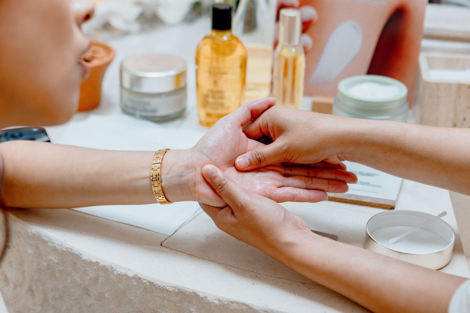Manicurist performing a hand massage with beauty products in the background at a nail salon.