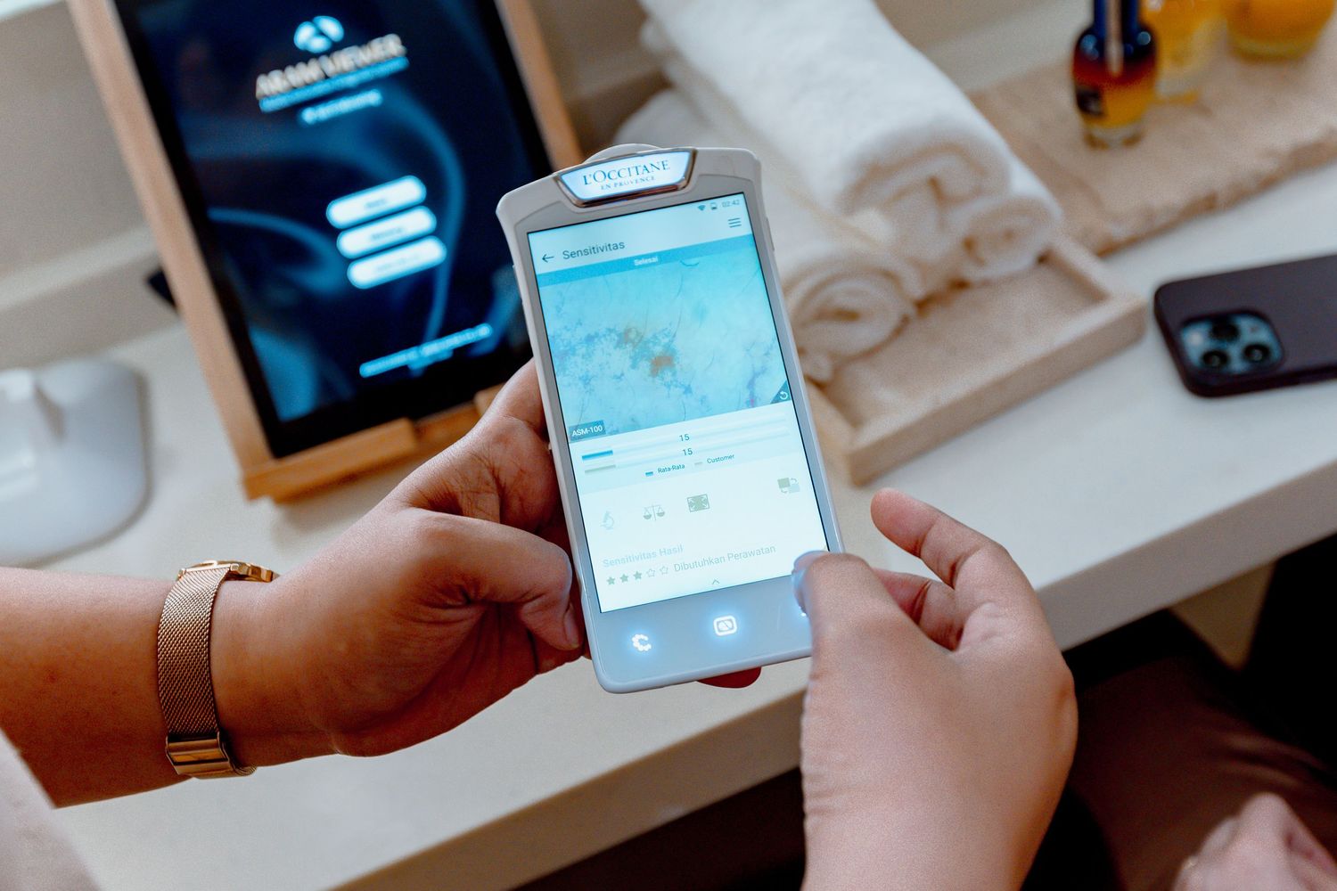 Person holding a smartphone displaying a map app, with a tablet and folded towels in the background.