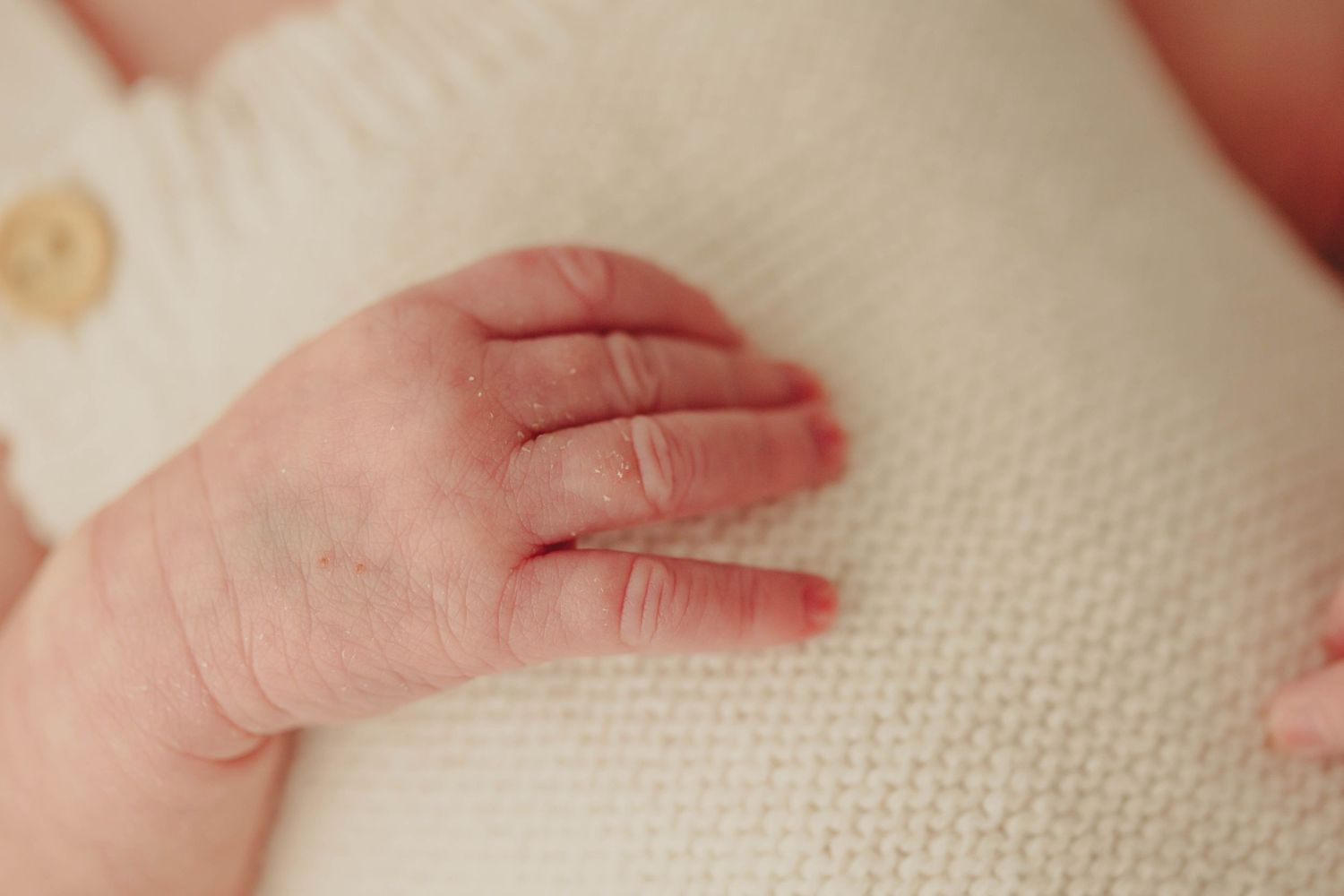 Close-up of a newborn baby's tiny hand resting on a soft white knit blanket.