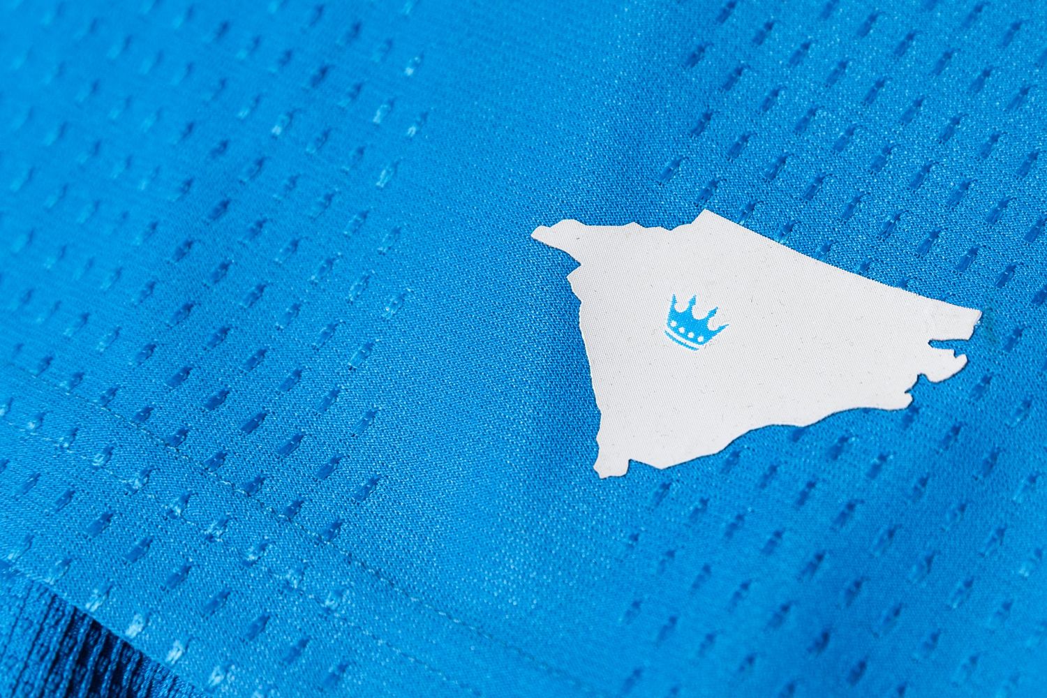 White outline of North Carolina state with Charlotte FC crown logo on blue jersey.