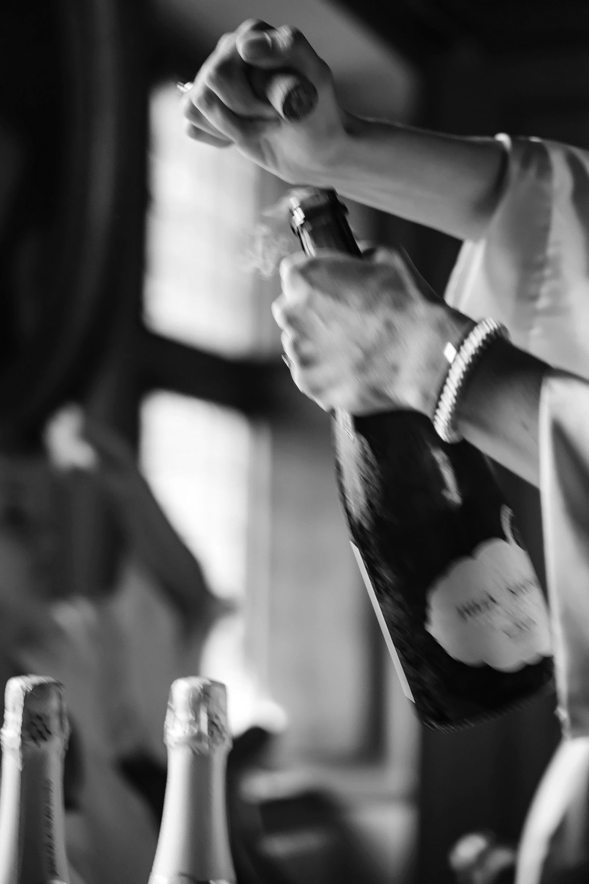 Champagne öppnas under ett bröllop, en svartvit bild i rörelse med oskärpa. Detaljfotografering av bröllopsfotograf Josefin Landhagen.