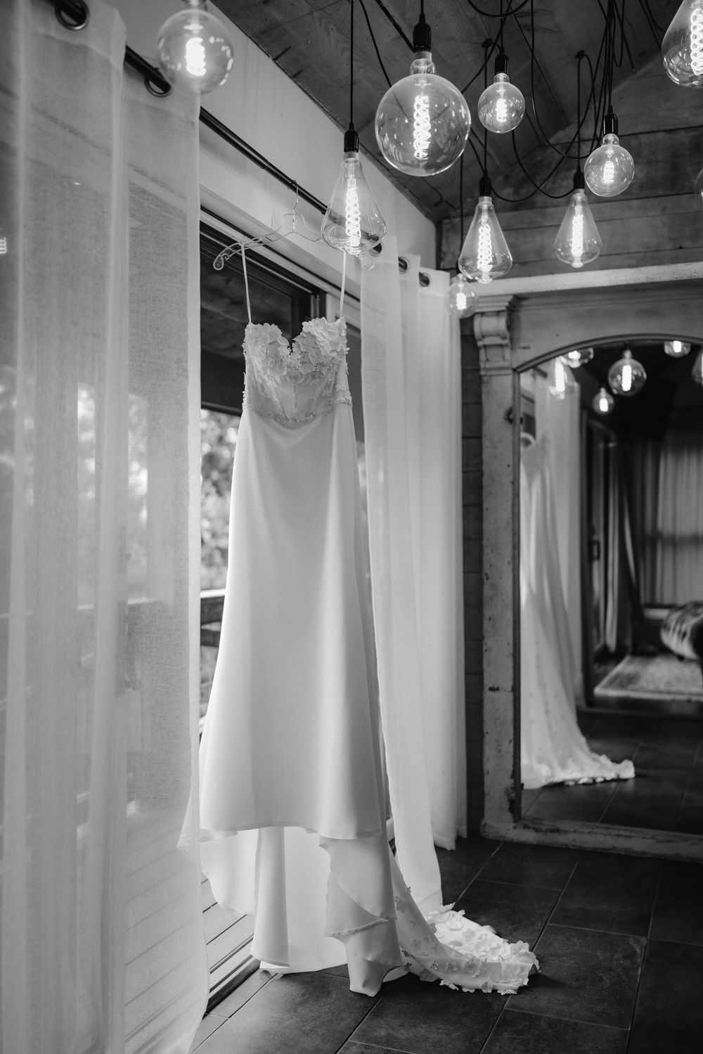 White wedding dresses hang from the ceiling in a dimly lit retail space with glass pendant lights.
