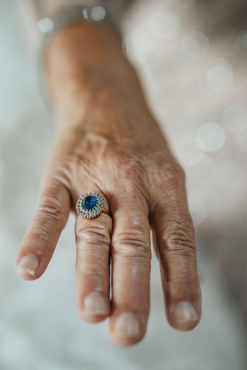 Close-up view of a vintage-style blue topaz ring with ornate silver setting displayed on a hand against blurred background.