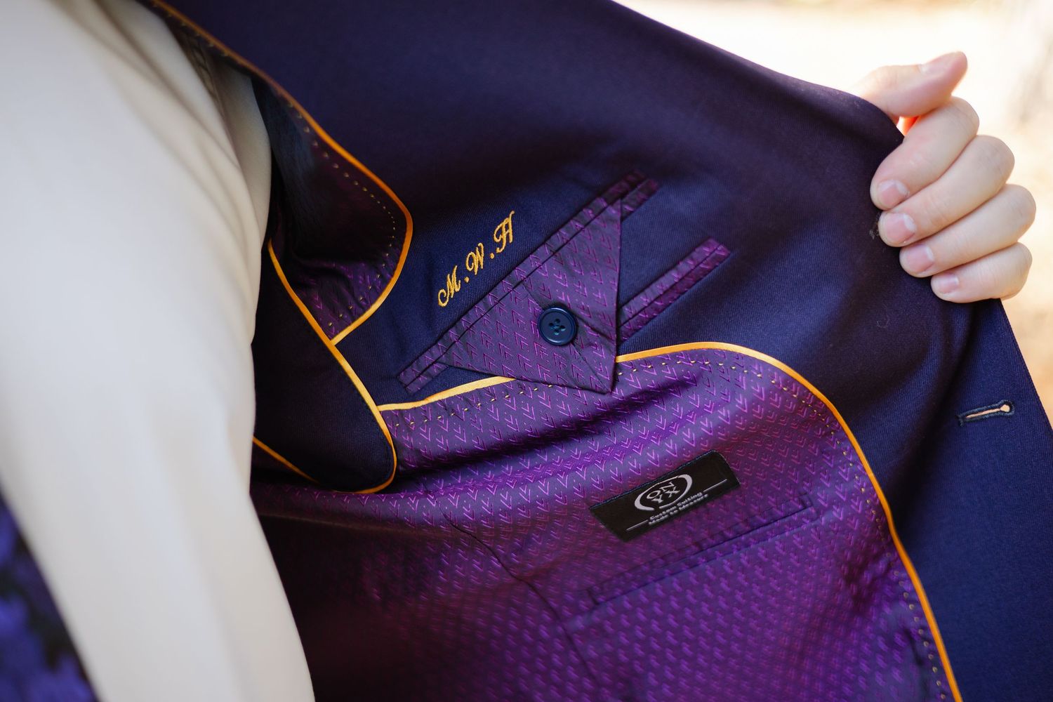 Close-up detail of a navy blue suit jacket with purple lining and orange piping showing craftsmanship details.