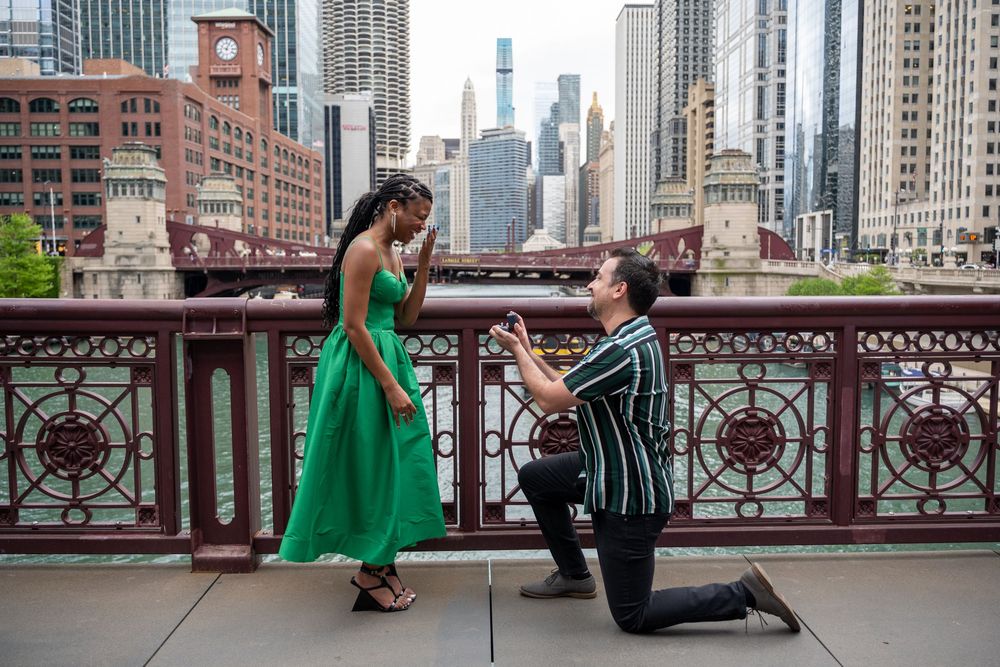 A couple shares a romantic proposal moment on a Chicago bridge with the city skyline in the background.