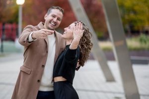 A joyful couple shares a candid moment laughing together outdoors while wearing autumn attire.