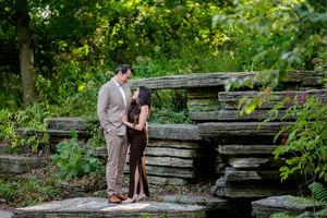 A romantic couple shares a tender moment on rustic stone steps surrounded by lush green foliage in a garden setting.