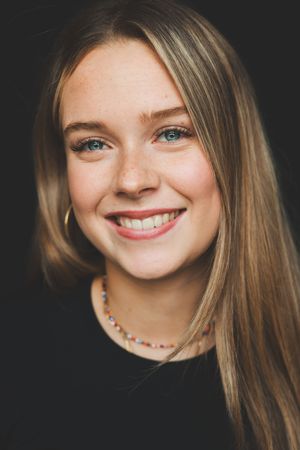 Smiling young blonde woman with blue eyes and freckles wearing a black top and colorful beaded necklace.