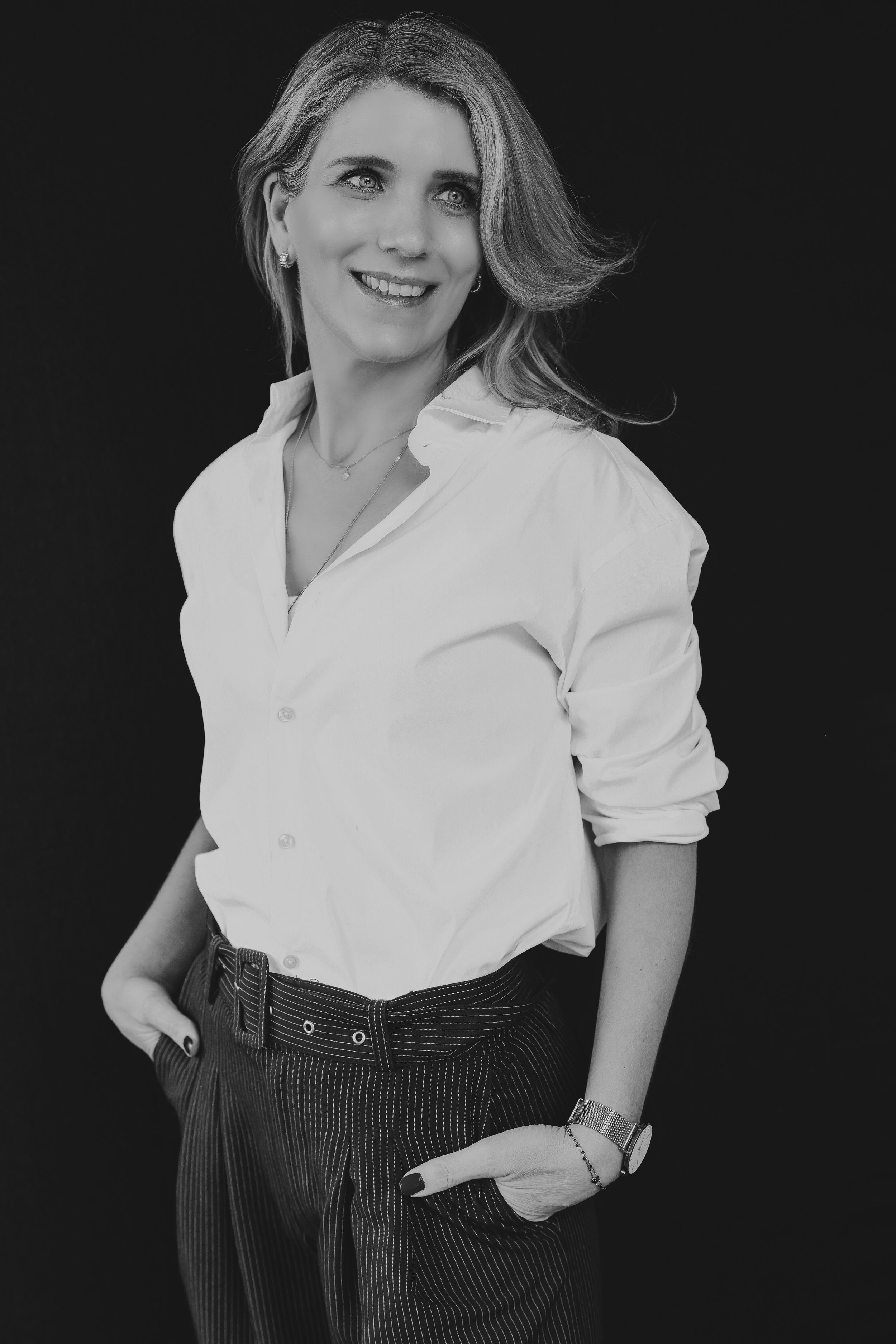 Black and white portrait of a smiling blonde woman in a white shirt and striped pants against dark background.