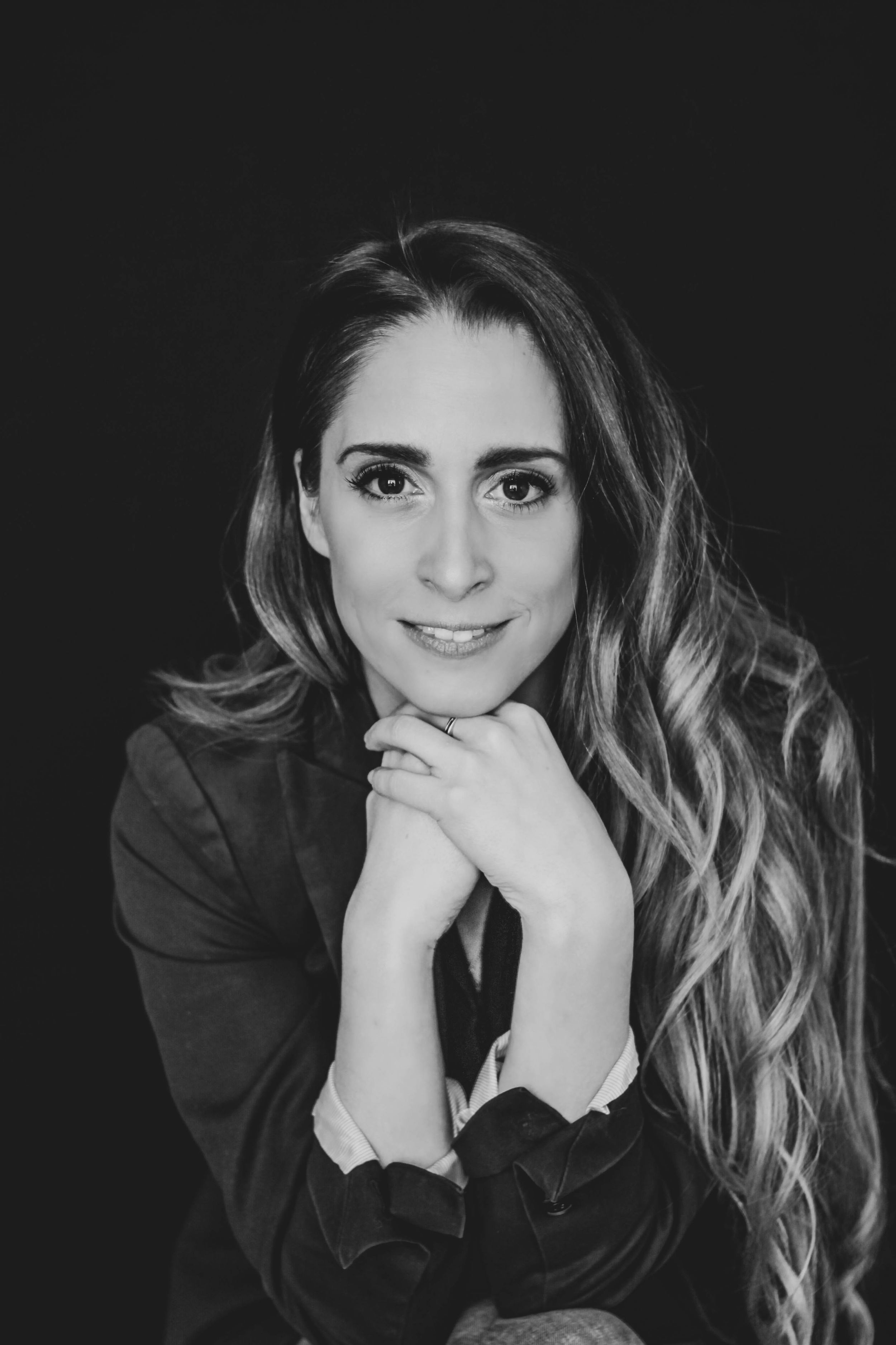 Black and white portrait of a smiling woman with long wavy hair resting chin on hands.