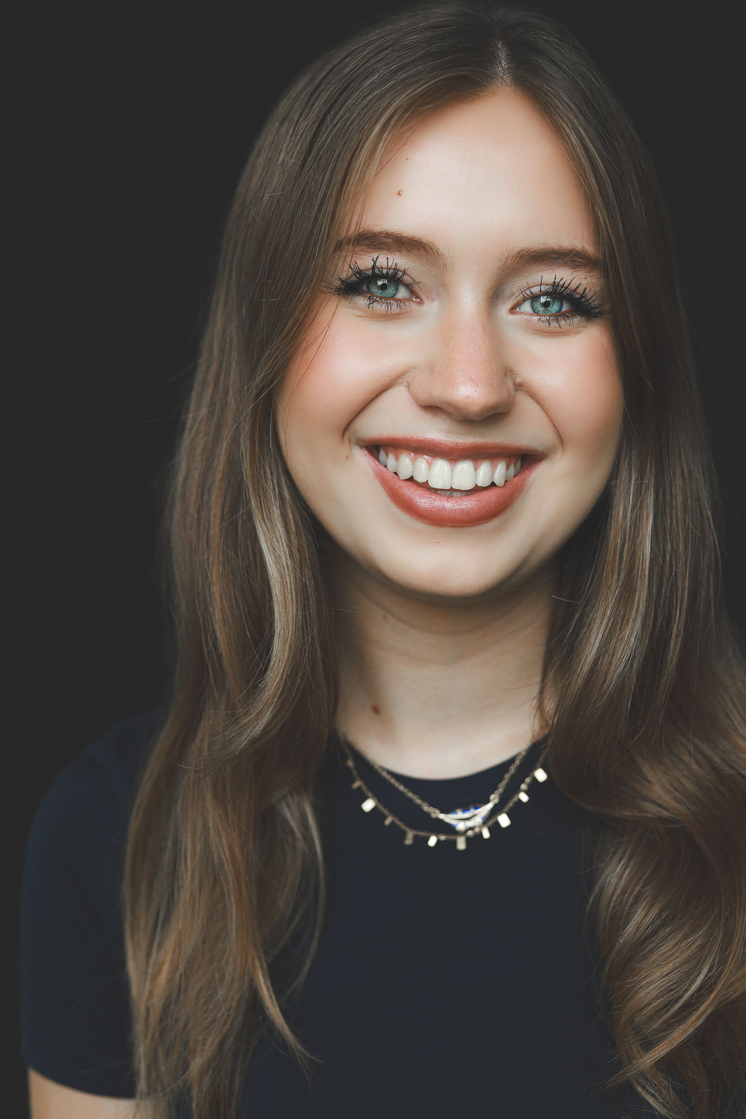 Headshot of a smiling young blonde woman with blue eyes wearing a black top and layered necklaces.